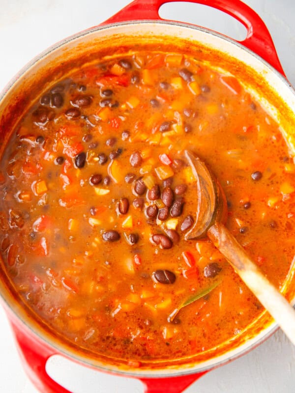 Hearty black bean soup simmering in a red Dutch oven with visible vegetables and a wooden spoon.