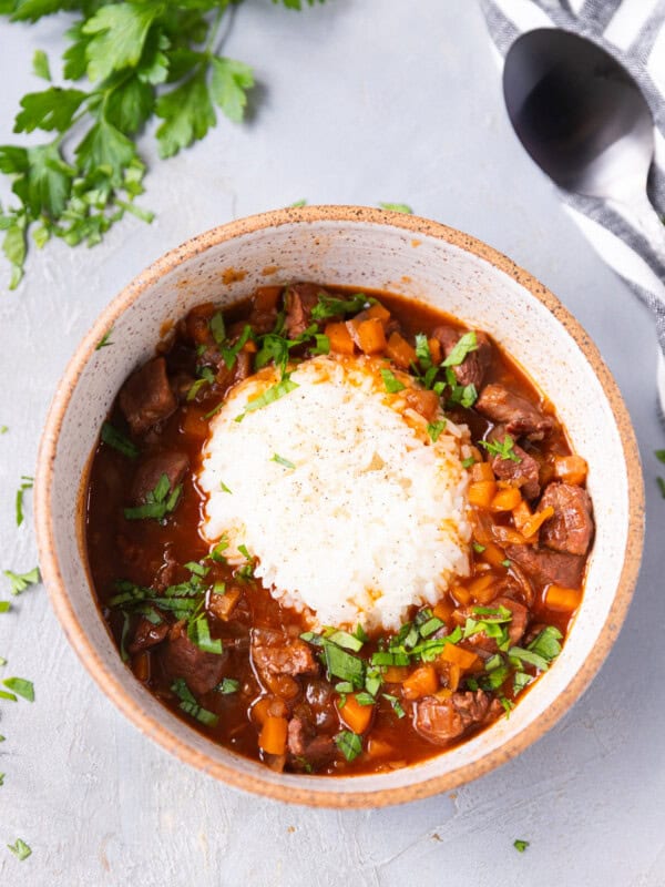 Bowl of Bulgarian beef stew with red wine served over white rice, topped with fresh parsley.