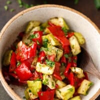 Bowl of roasted zucchini and red peppers garnished with parsley.