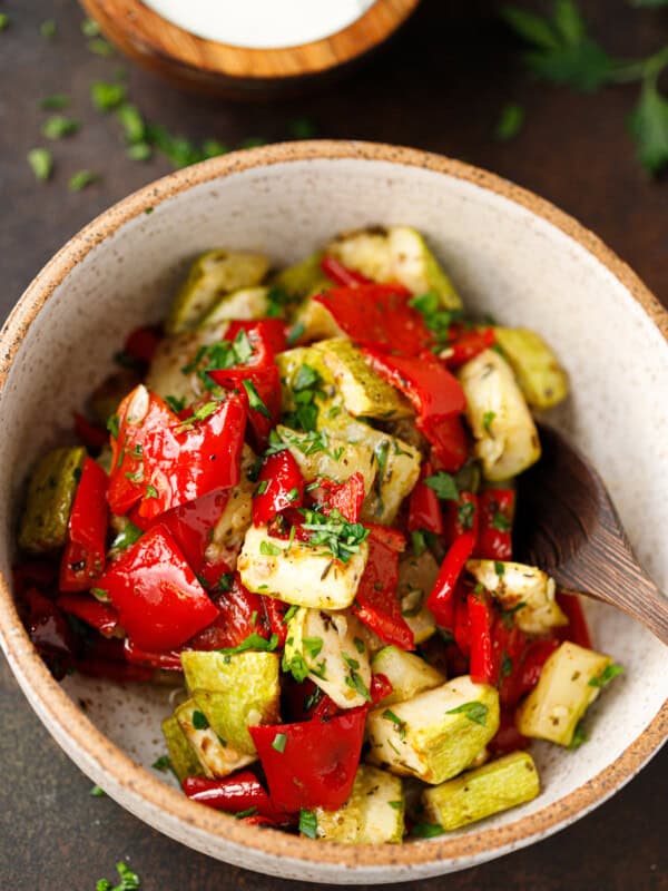 Bowl of roasted zucchini and red peppers garnished with parsley.