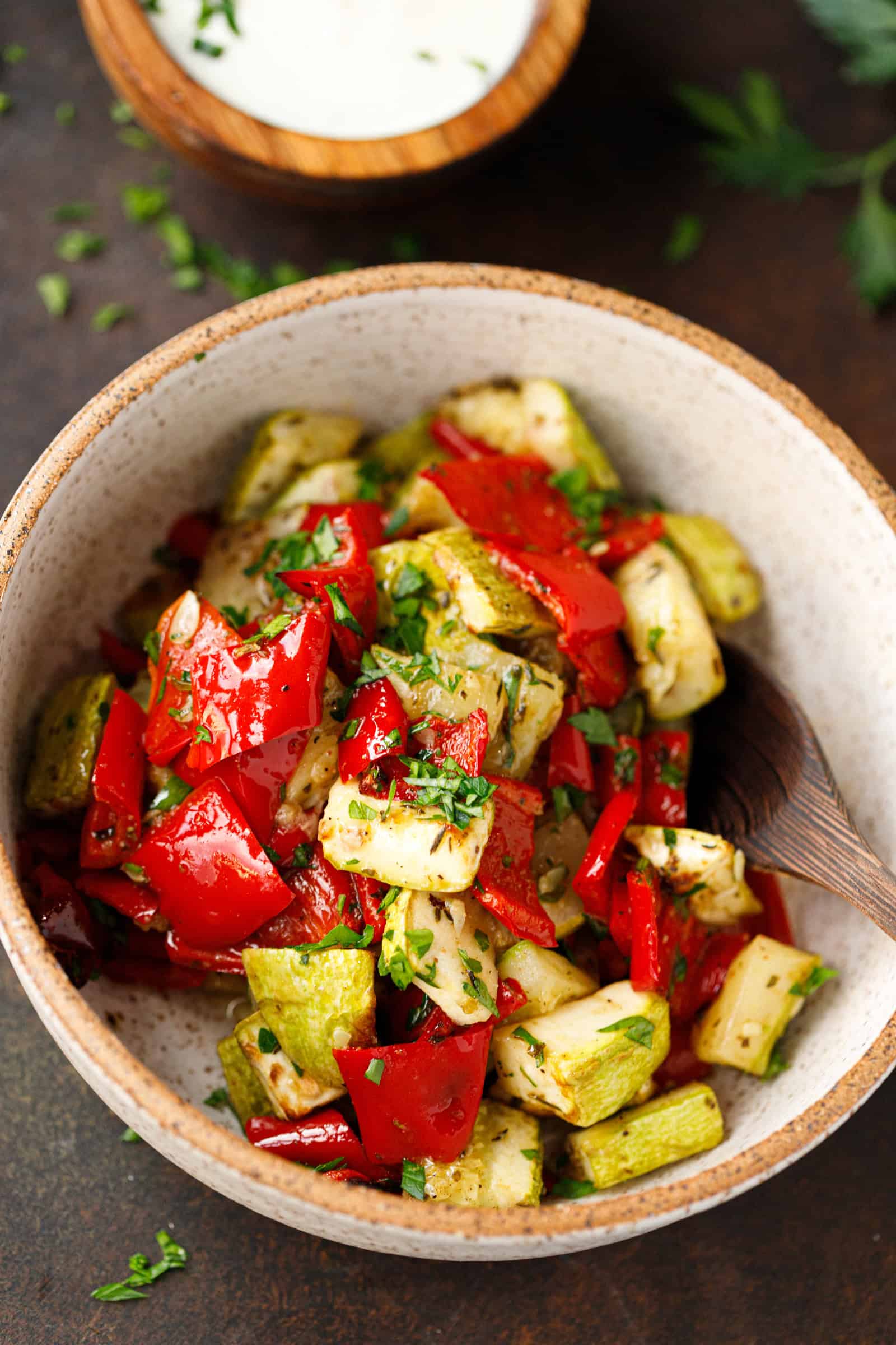 Bowl of roasted zucchini and red peppers garnished with parsley.