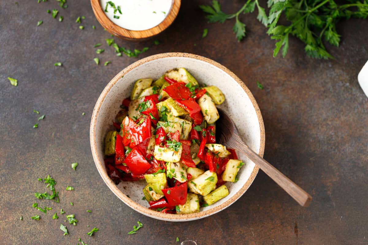 Roasted zucchini and peppers in a speckled bowl with a wooden spoon.