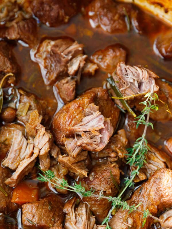 Fork holding a tender piece of braised beef with carrots over creamy mashed potatoes