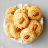 Soft keto almond cookies topped with whole almonds, stacked on a white plate.