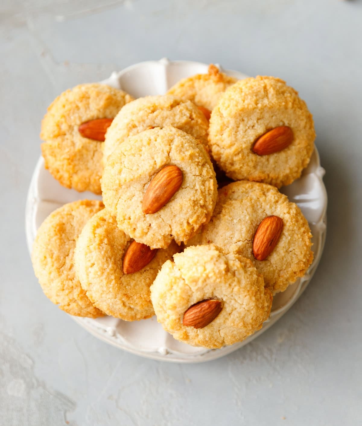 Soft keto almond cookies topped with whole almonds, stacked on a white plate.
