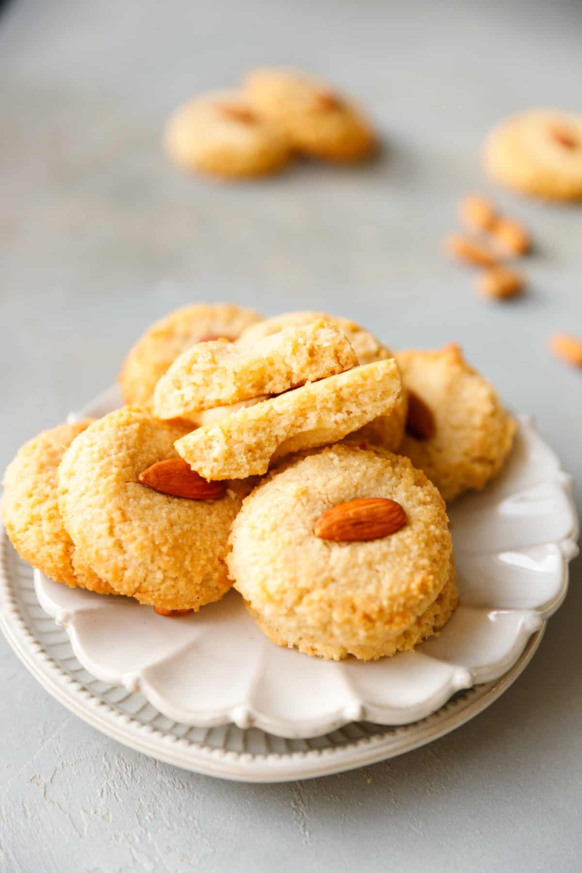 Stack of keto almond cookies on a white plate, showing crisp edges and whole almond topping.