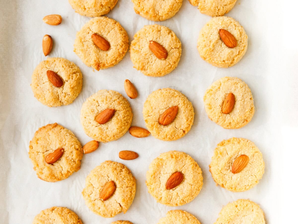 Baked keto almond cookies topped with whole almonds arranged on parchment paper.