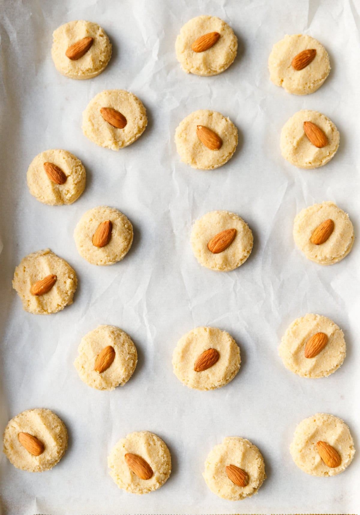 Unbaked keto almond cookies topped with whole almonds arranged on a parchment-lined baking sheet.