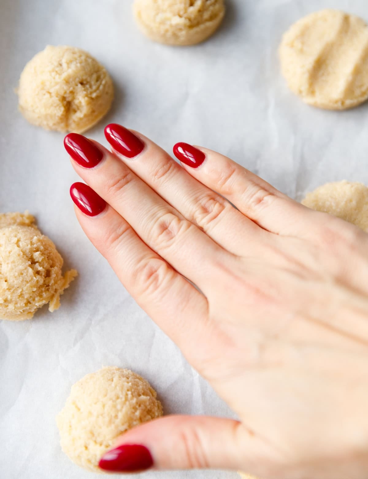 Hand flattening scooped keto almond cookie dough balls on a parchment-lined baking sheet.