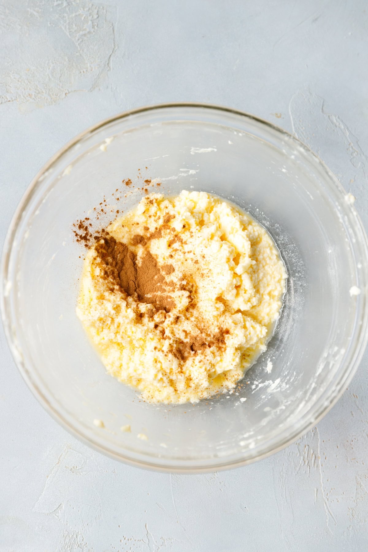 Cinnamon sprinkled over the mixed wet ingredients in a glass bowl.