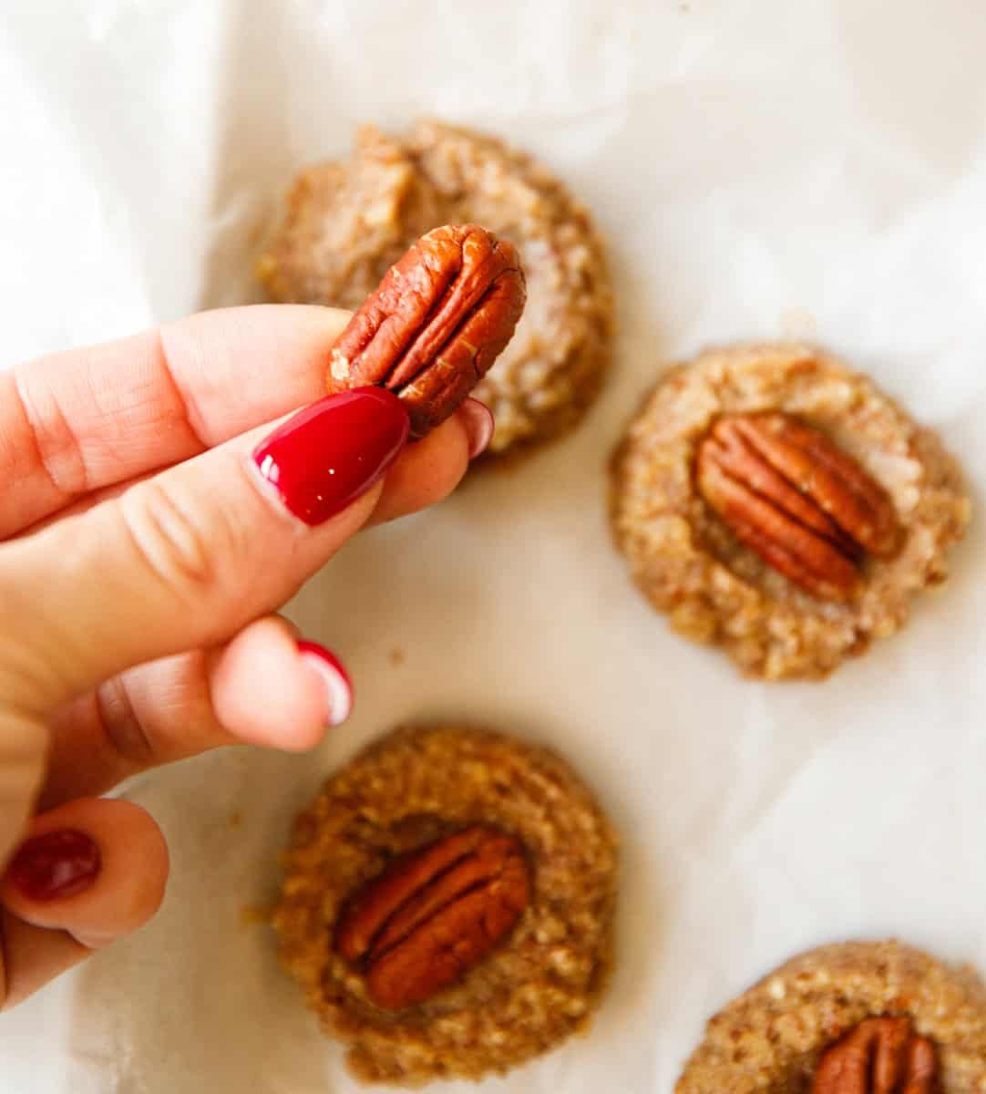 Hand holding a whole pecan above unbaked maple pecan cookies on parchment