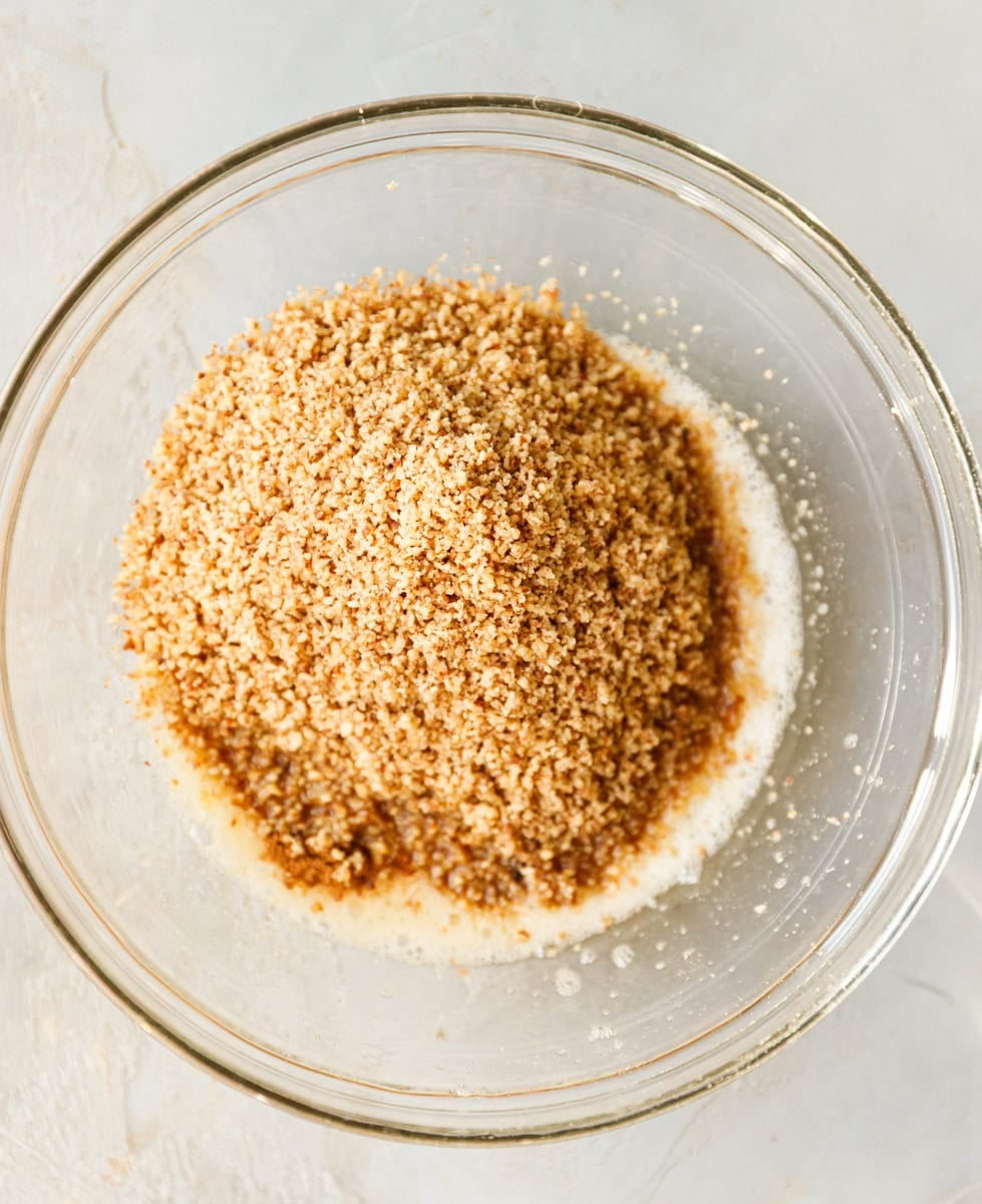 Bowl filled with ground pecans poured over whisked egg white and maple syrup
