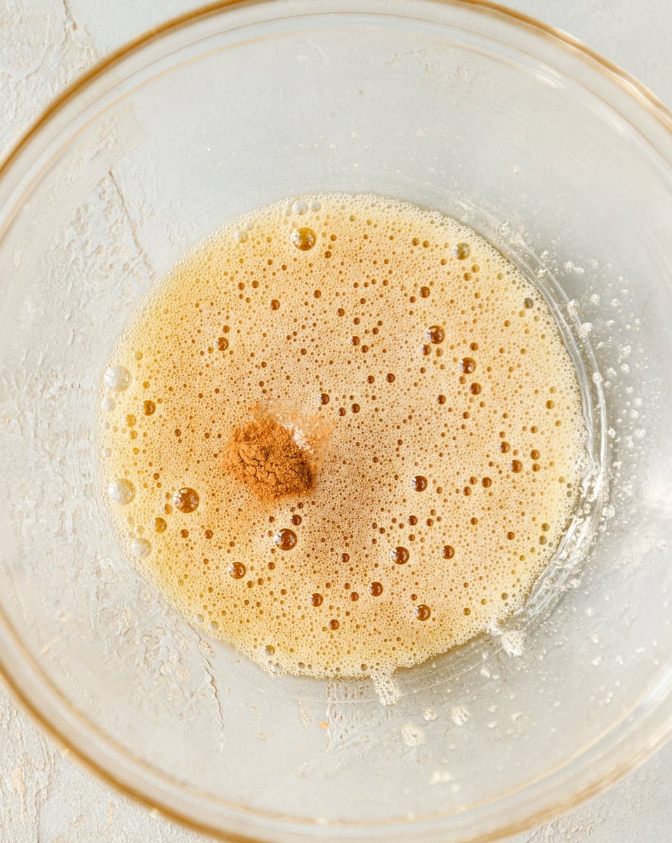 Whisked egg white with cinnamon in a glass bowl for maple pecan cookie batter