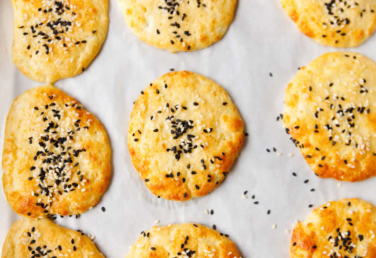 Low-carb cottage cheese flatbreads baking on parchment paper with sesame seeds