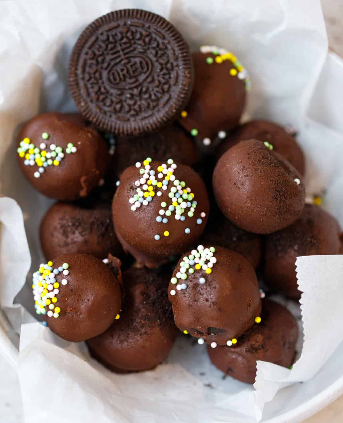 Chocolate Oreo truffles coated in dark chocolate with sprinkles in a white bowl