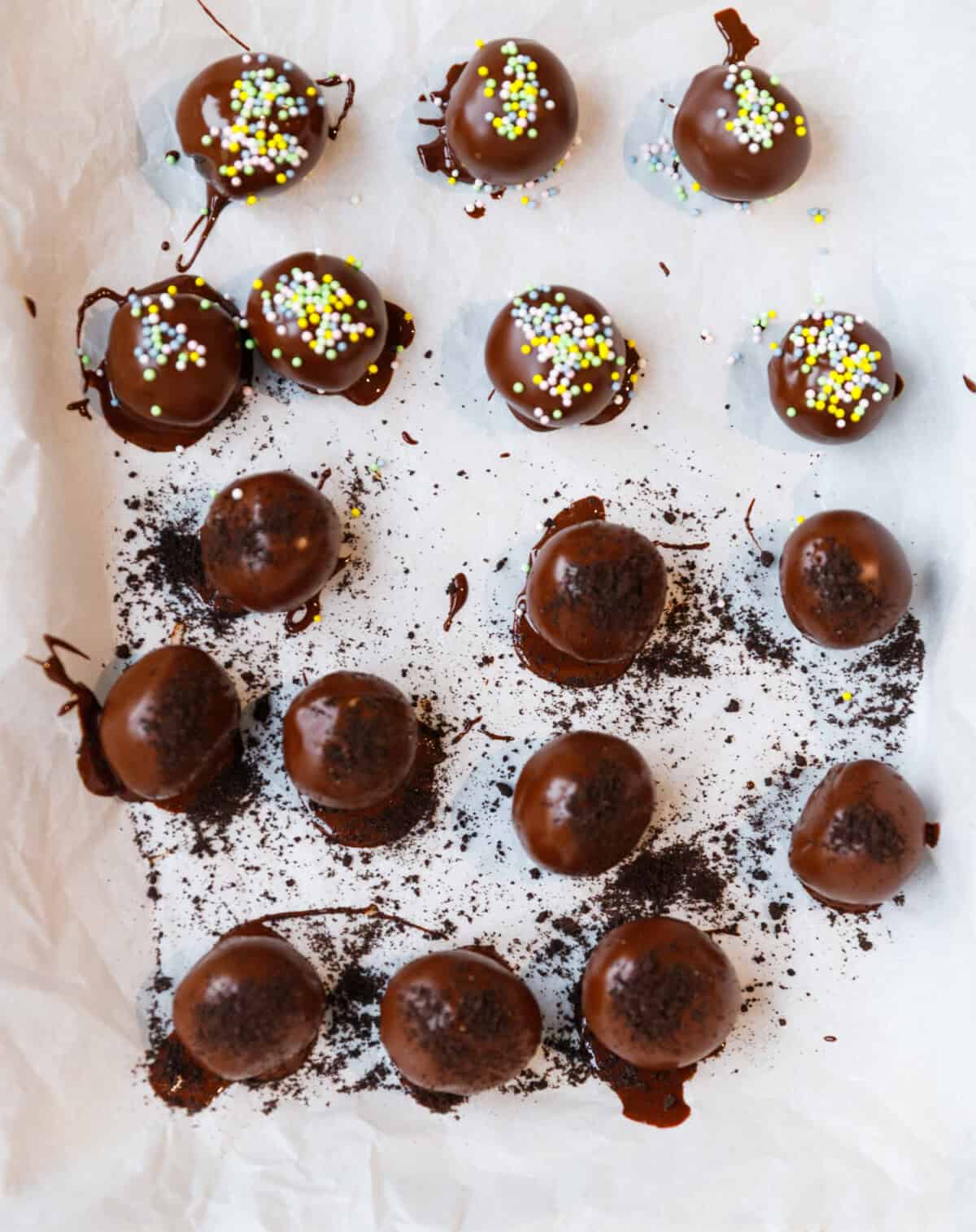Chocolate-dipped Oreo truffles setting on parchment with sprinkles and Oreo crumbs