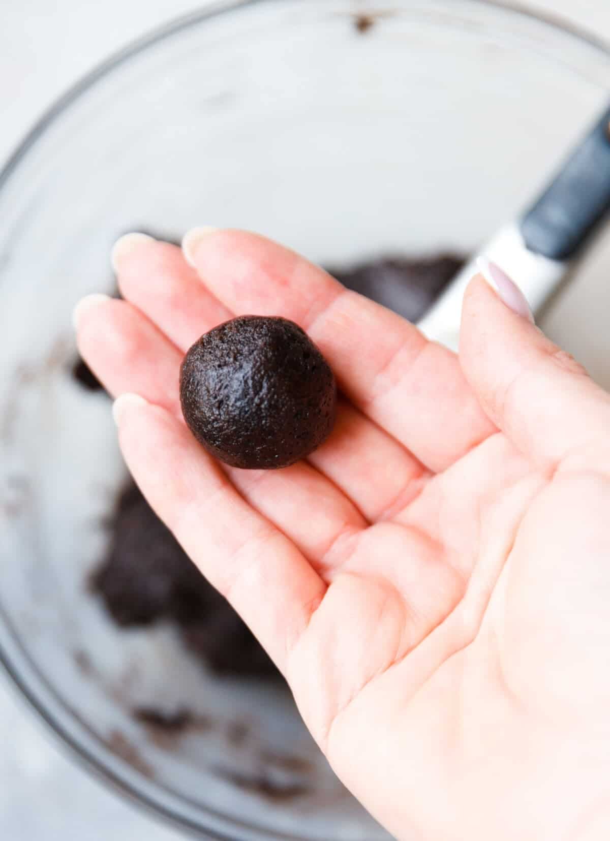 Hand holding a rolled Oreo truffle ball over the mixing bowl