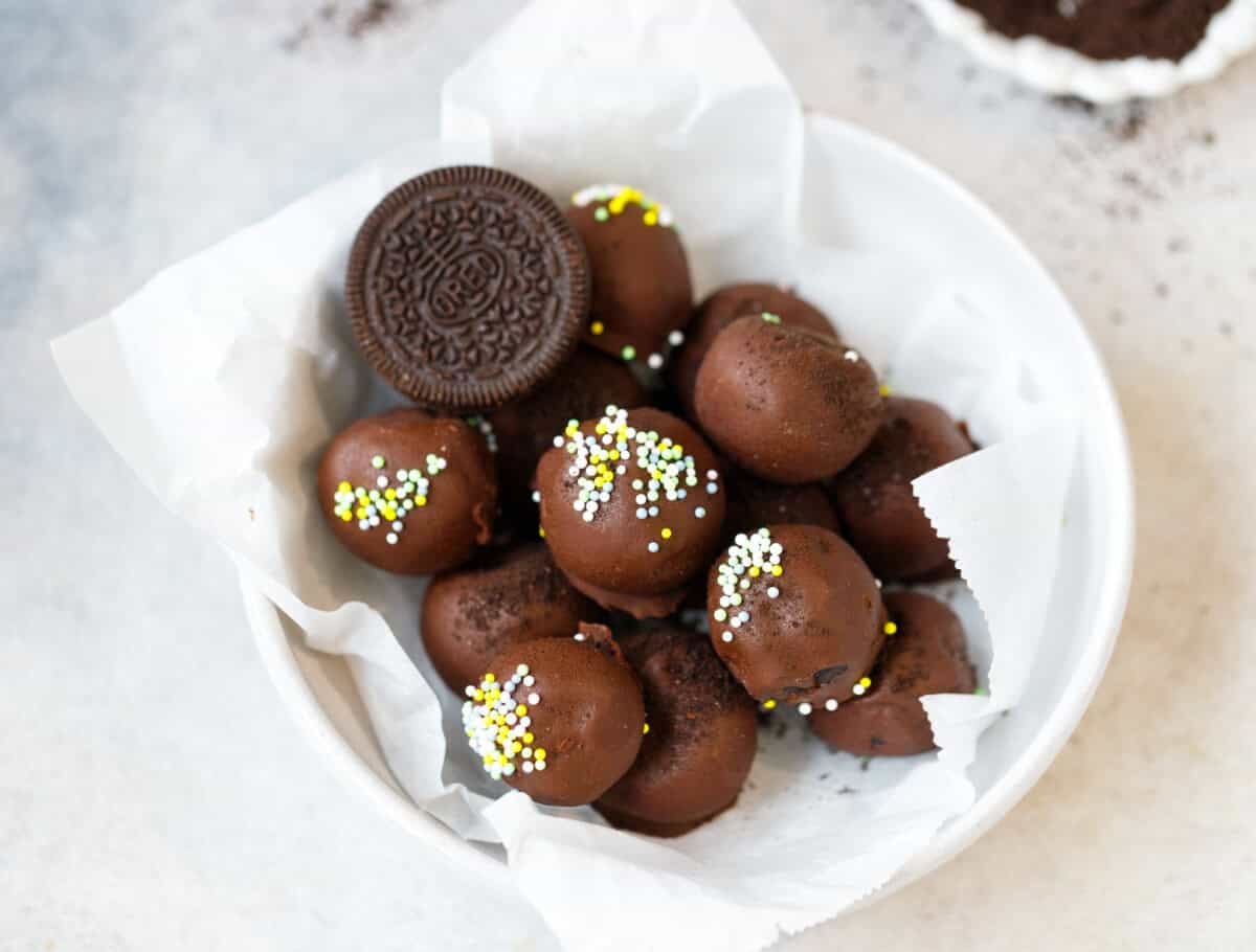 Overhead view of chocolate Oreo truffles in a white bowl lined with parchment paper