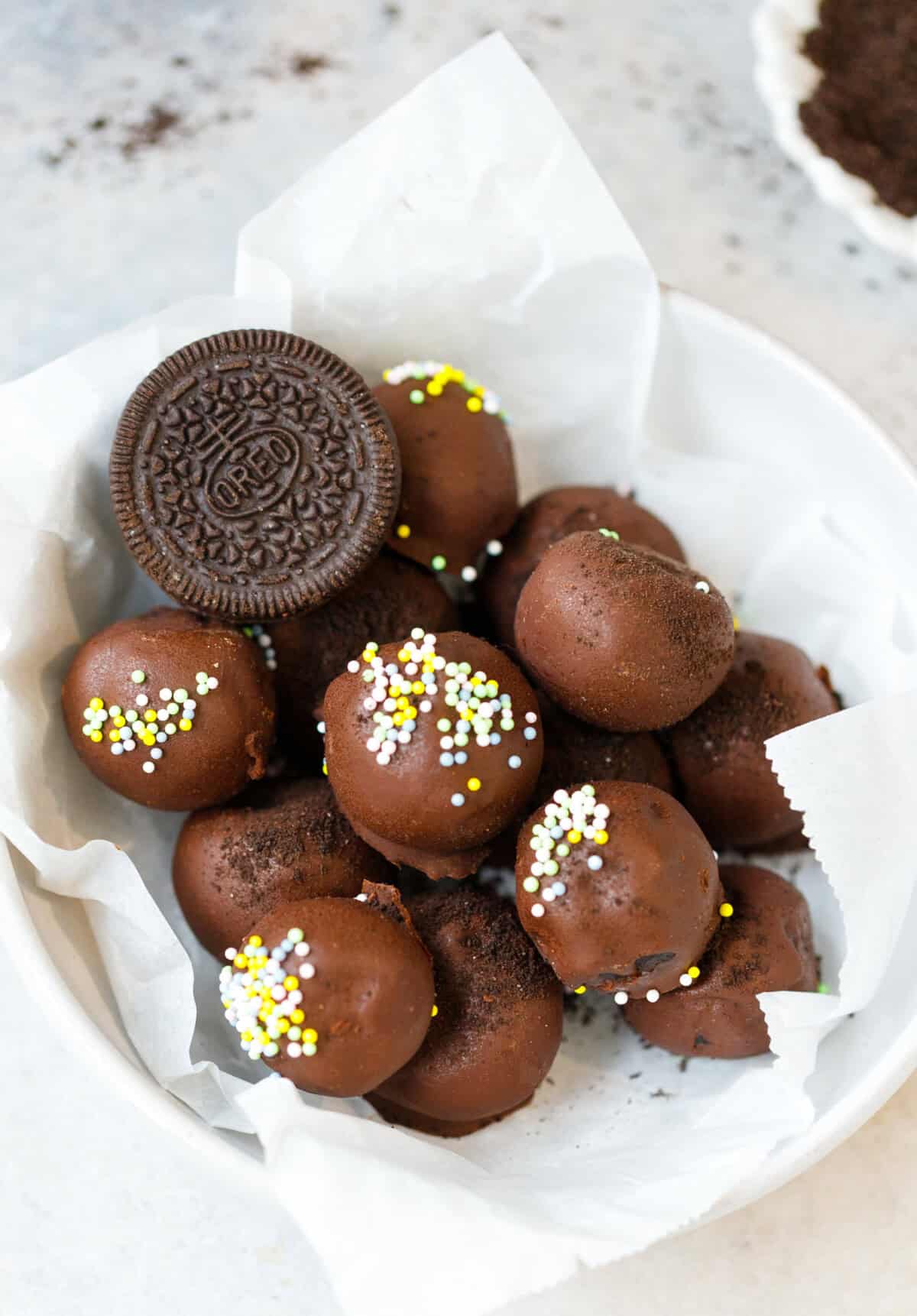 Chocolate Oreo truffles coated in dark chocolate with sprinkles in a white bowl