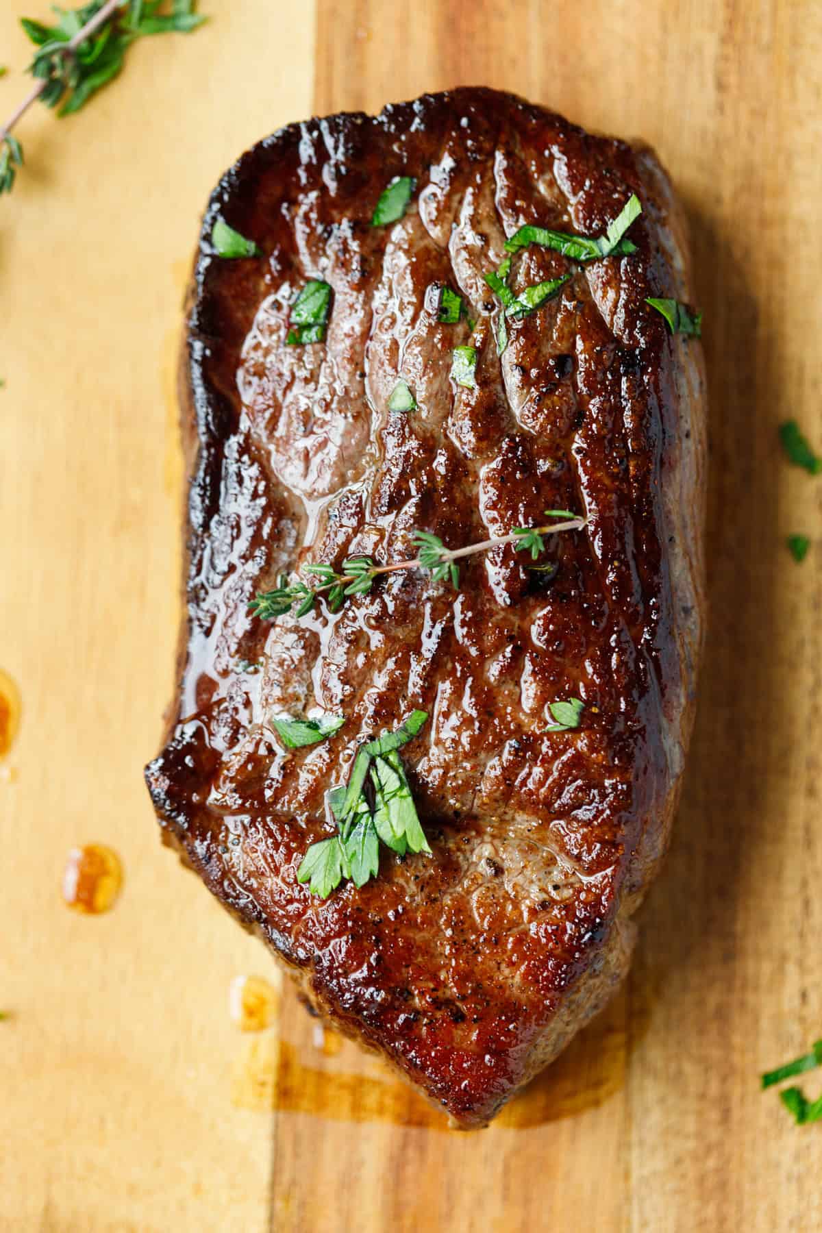 Cooked Denver steak resting on wooden cutting board with fresh herbs.
