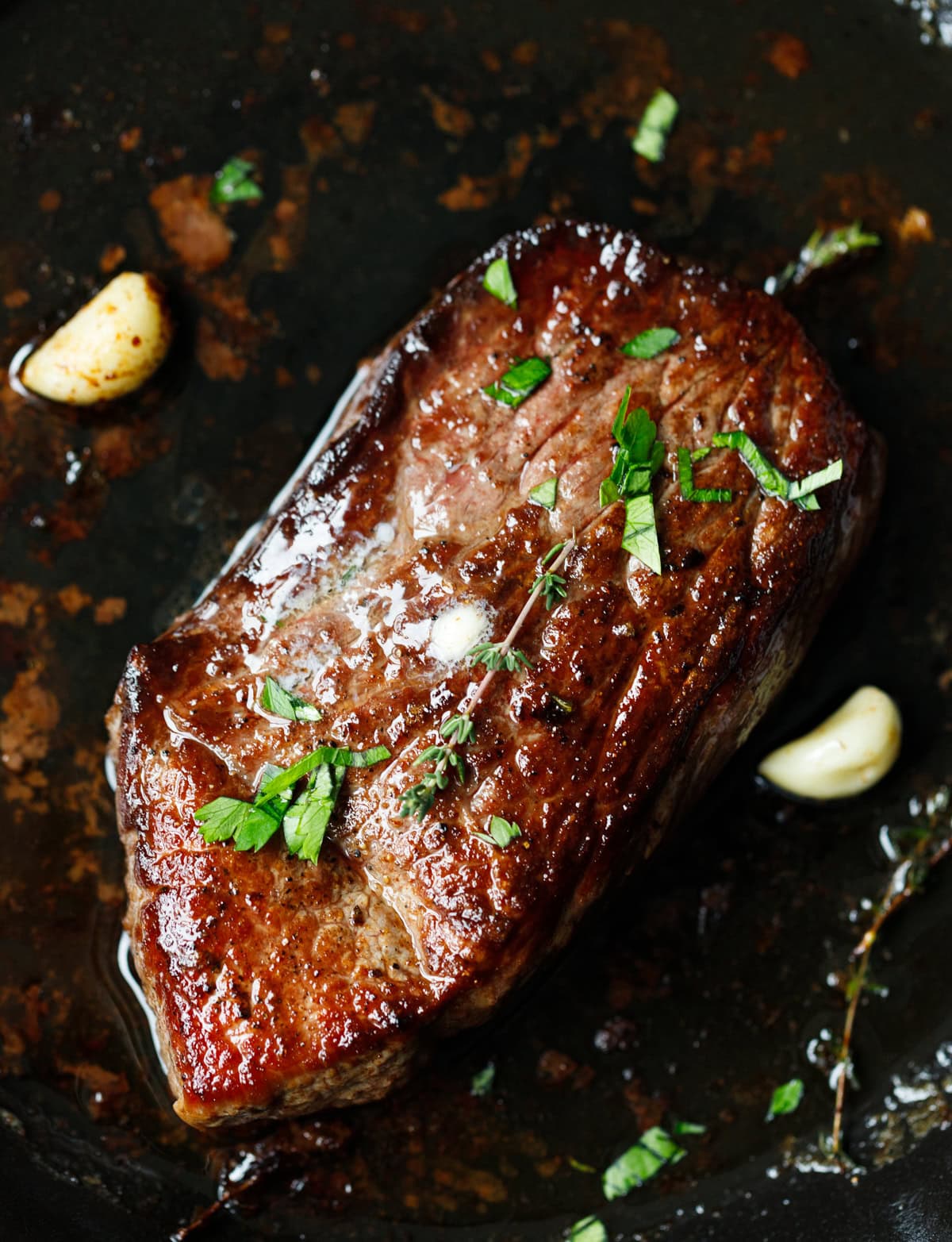 Pan-seared Denver steak with melted butter, garlic, and herbs in skillet.