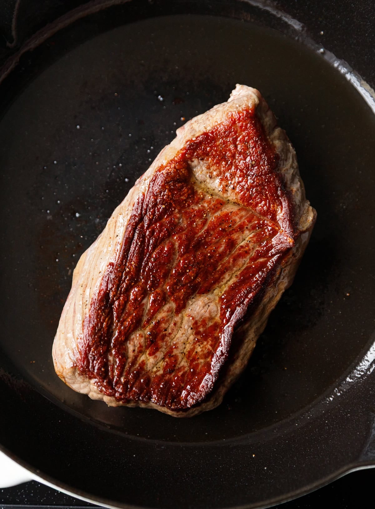 Seared Denver beef steak inside a skillet, flipped to cook both sides.