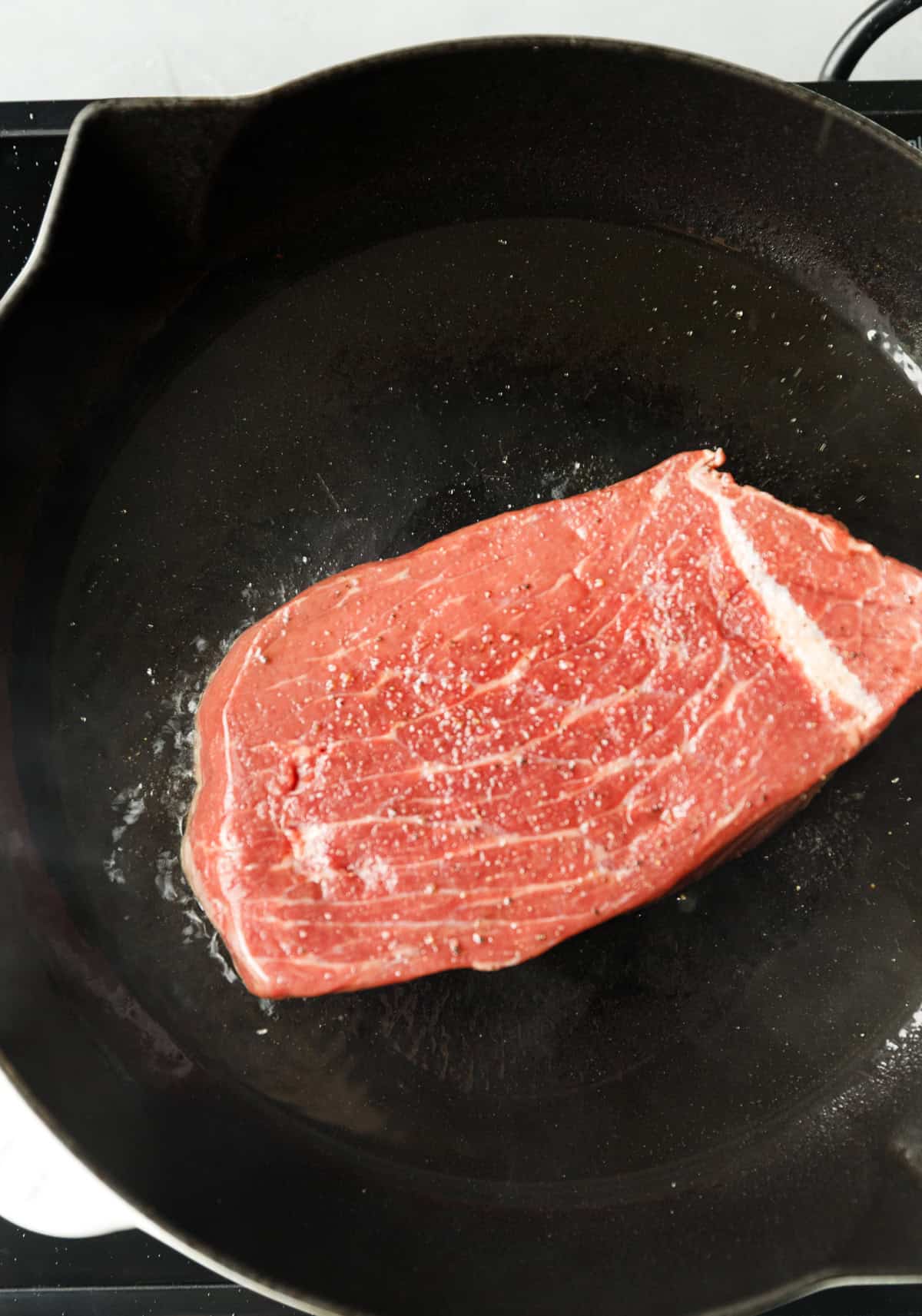 Raw Denver steak inside a hot pan being seared