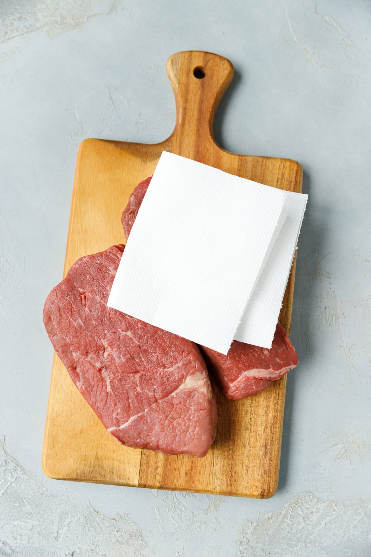 Two Denver steaks on a wooden board patted dry with kitchen paper