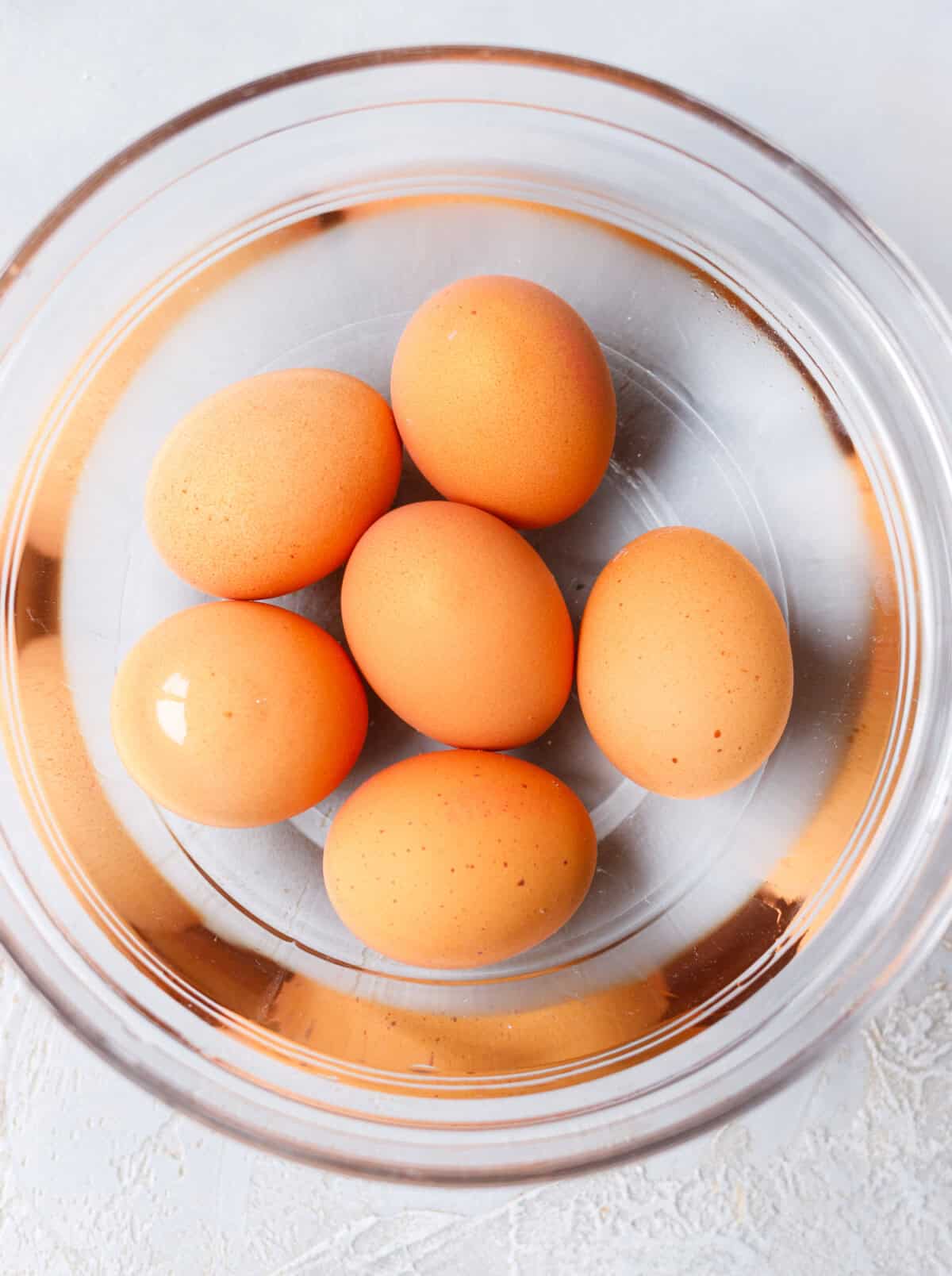 Boiled eggs in glass bowl with cold water for making deviled eggs with pickles