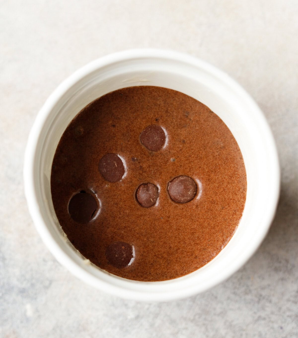 Chocolate collagen cake batter with chocolate chips in a white ramekin before baking