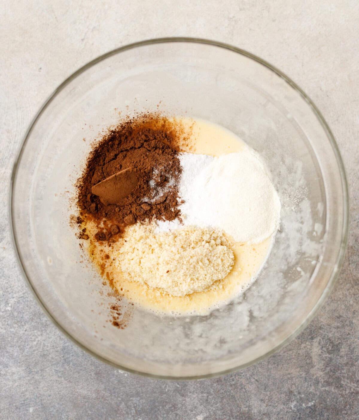 Cocoa powder, almond flour, collagen, and sweetener added to wet ingredients in a bowl