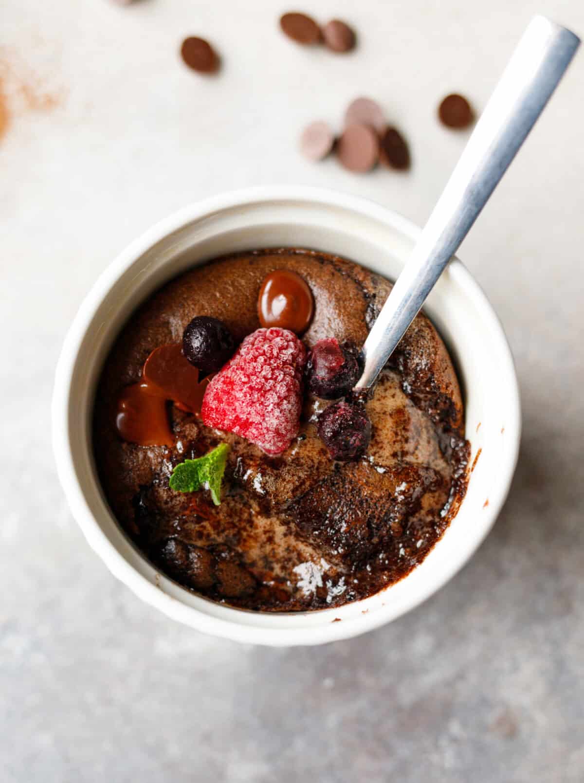 Low-carb chocolate collagen mug cake topped with berries and chocolate chips in a white ramekin