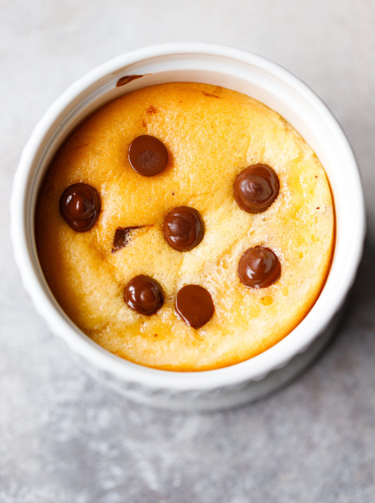 Single serve protein cake baked in a white ramekin with golden top and melted chocolate chips.