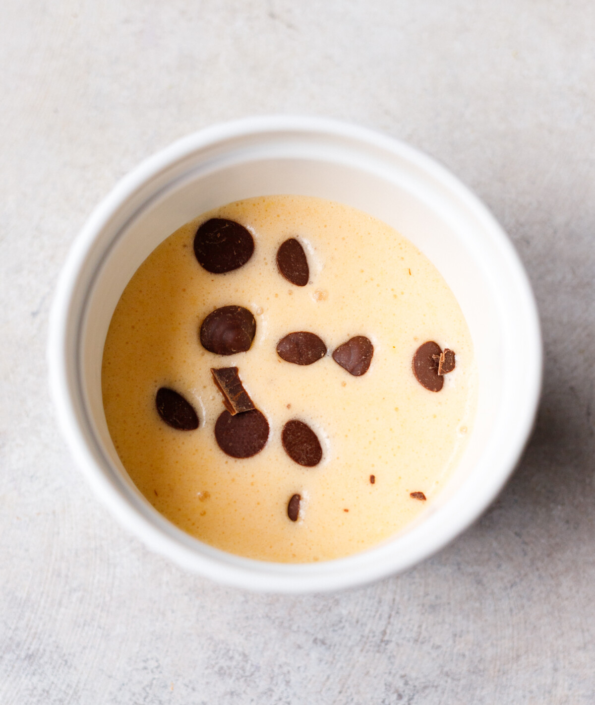 Single serve protein cake batter poured into a white ramekin and topped with chocolate chips before baking.