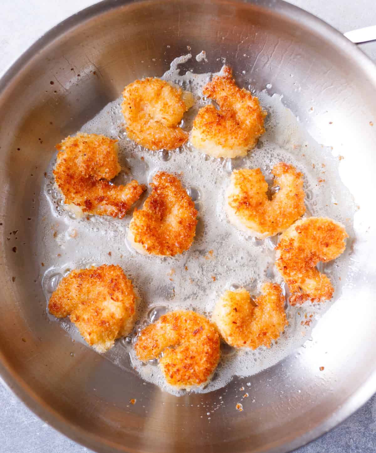 Coconut shrimp frying in a pan with oil until golden and crispy