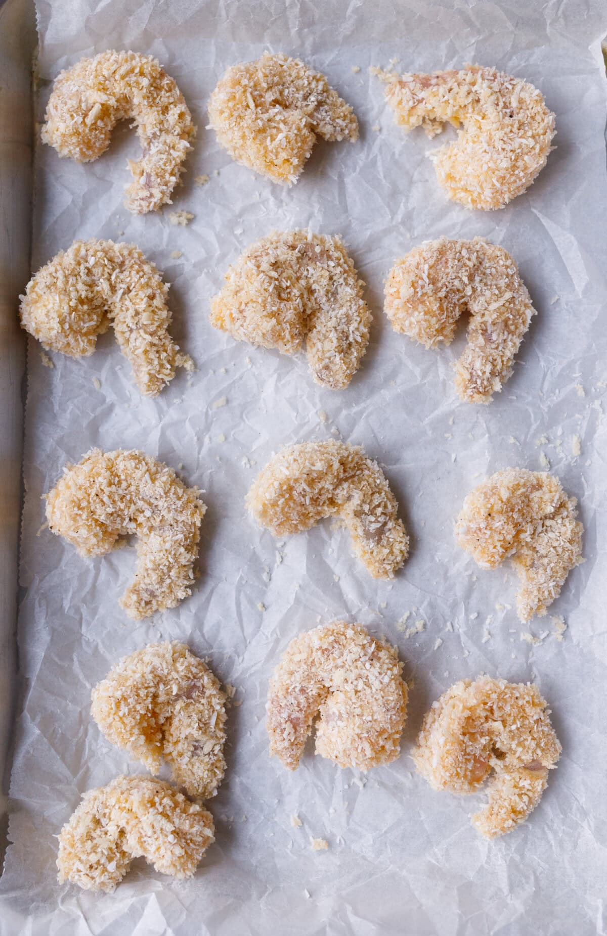 Breaded coconut shrimp arranged on baking sheet before cooking