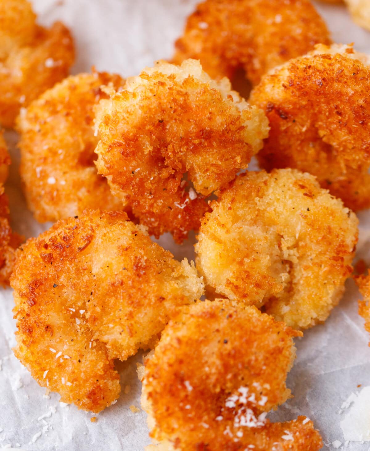 Golden crispy coconut shrimp on parchment paper with shredded coconut topping