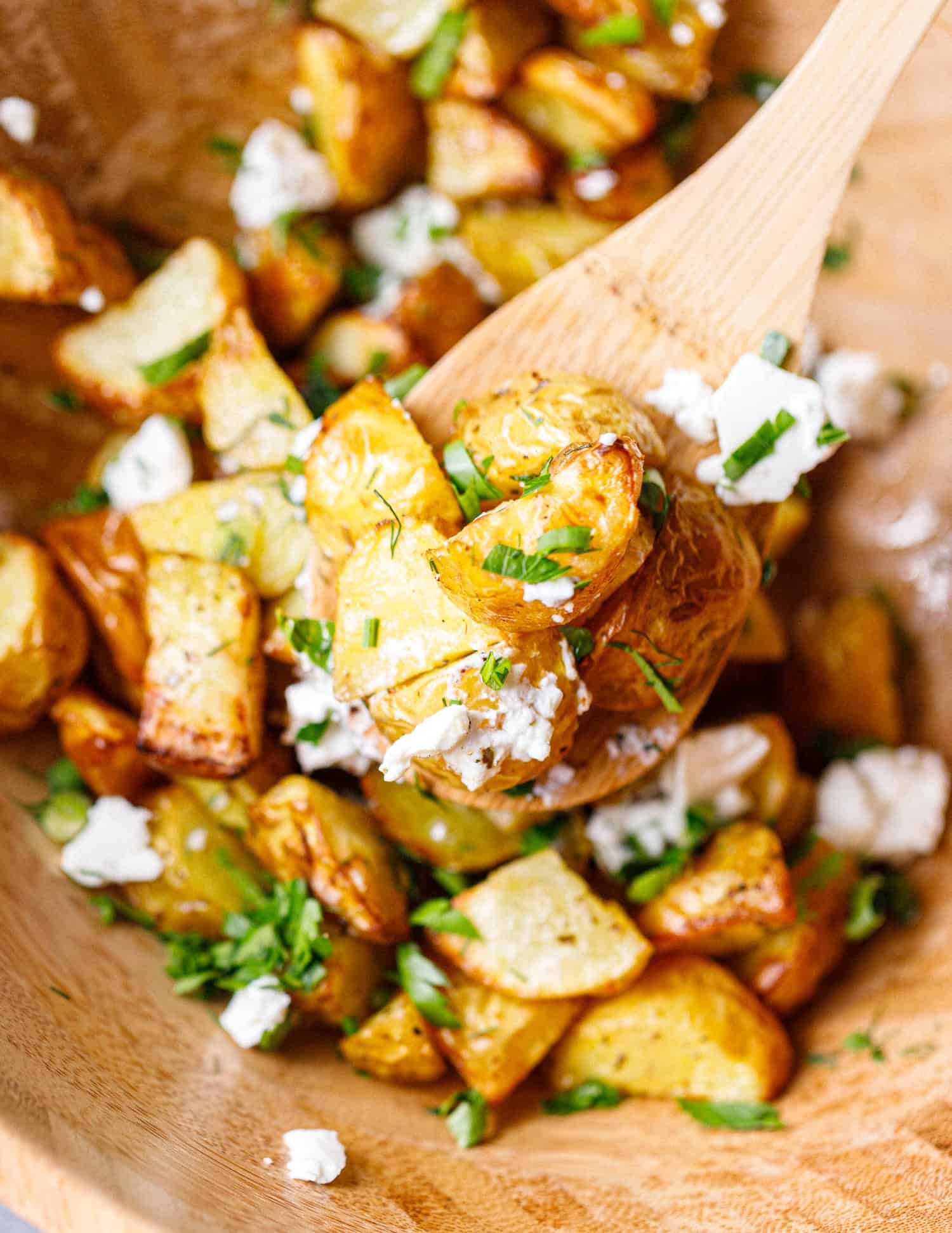 Close-up of a wooden spoon scooping crispy air fryer baby potatoes with feta and fresh herbs