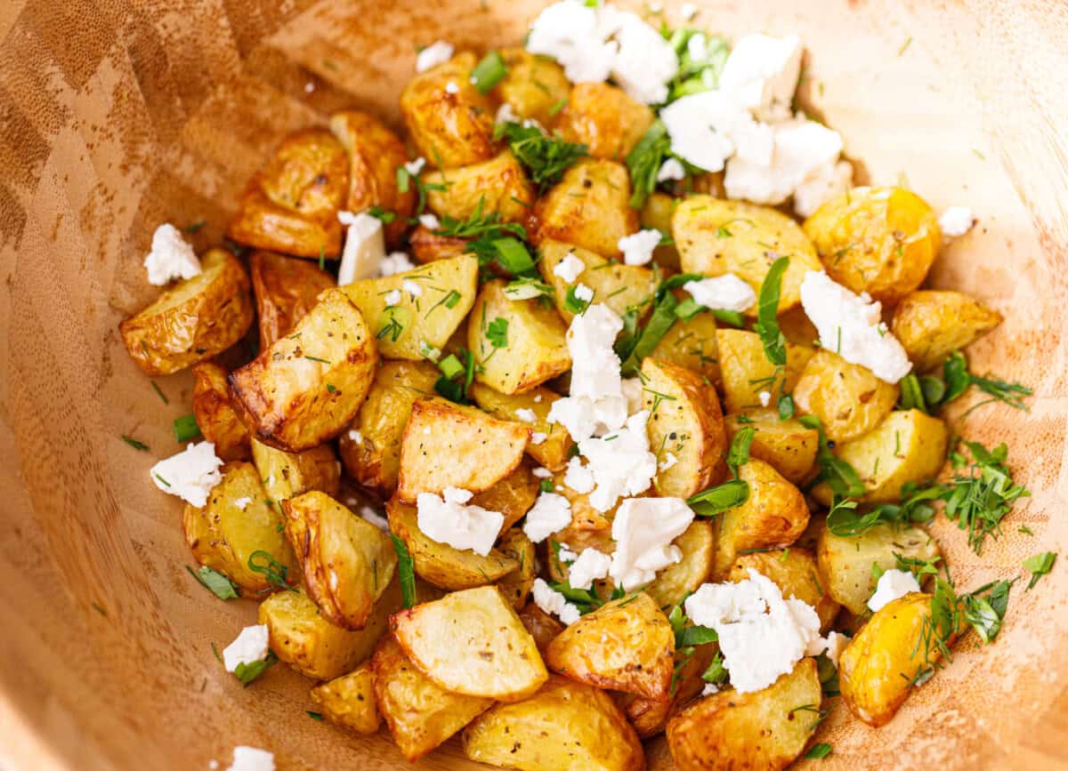 Air fryer baby potatoes topped with crumbled feta, dill, parsley, and sliced green onion in a wooden bowl