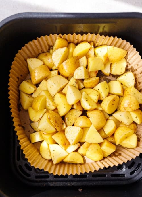Seasoned baby potato pieces arranged in a single layer in a parchment-lined air fryer basket
