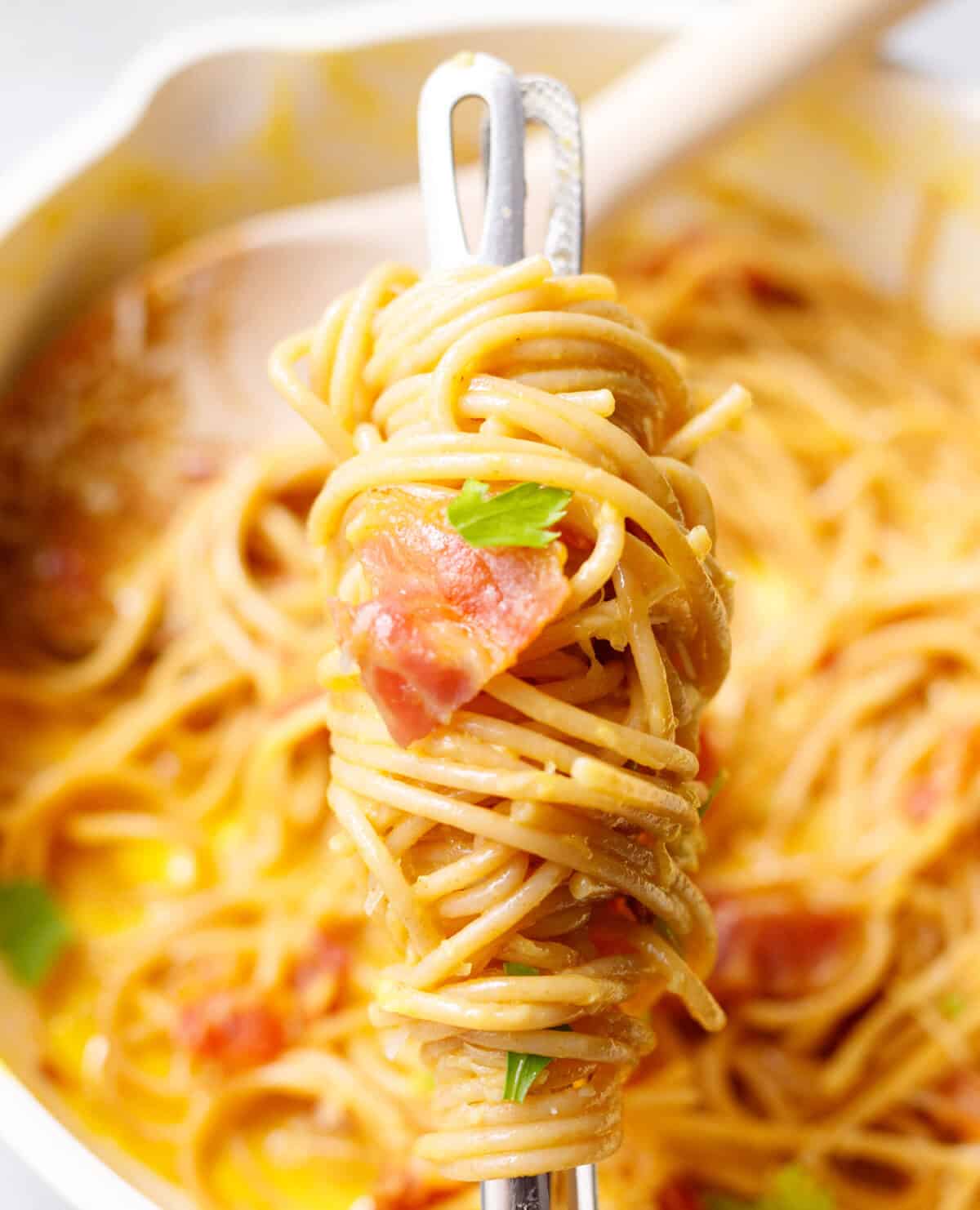 Fork twirling spaghetti carbonara with bacon and Parmesan over a pan of pasta.
