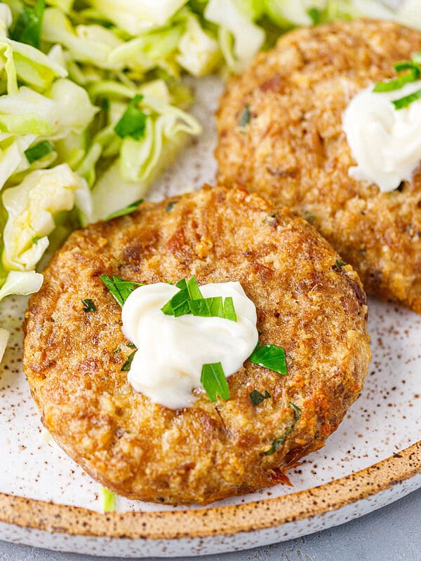 Canned tuna patties served on a speckled plate with cabbage salad and a dollop of sour cream