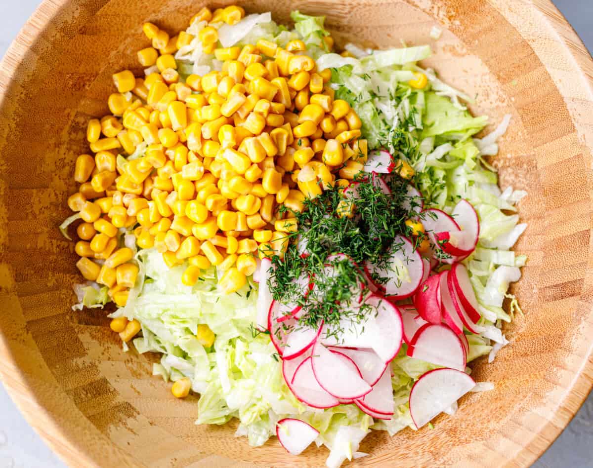  Iceberg lettuce salad with corn, sliced radishes, and fresh dill in a wooden bowl before tossing
