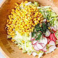 Iceberg lettuce salad with corn, sliced radishes, and fresh dill in a wooden bowl before tossing
