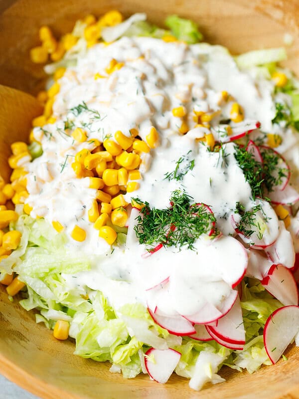 Creamy garlic yogurt dressing poured over iceberg lettuce salad with corn and radishes