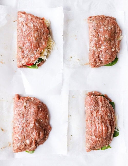 Ground turkey pocket being folded in half over the filling using parchment paper on a baking sheet