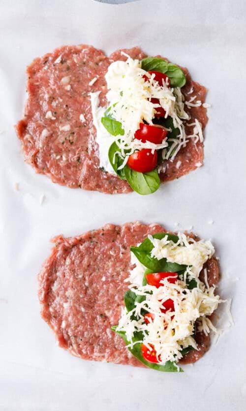Shredded mozzarella added over cream cheese, spinach, and cherry tomatoes on ground turkey ovals before folding