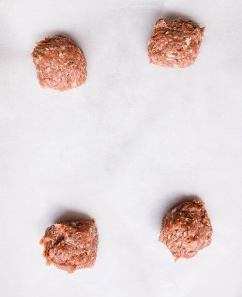 Four equal portions of seasoned raw ground turkey on parchment paper ready to be shaped