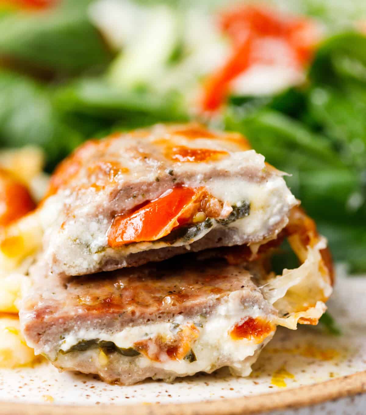 Ground turkey pockets cut in half showing creamy cheese and cherry tomato filling with green salad in the background