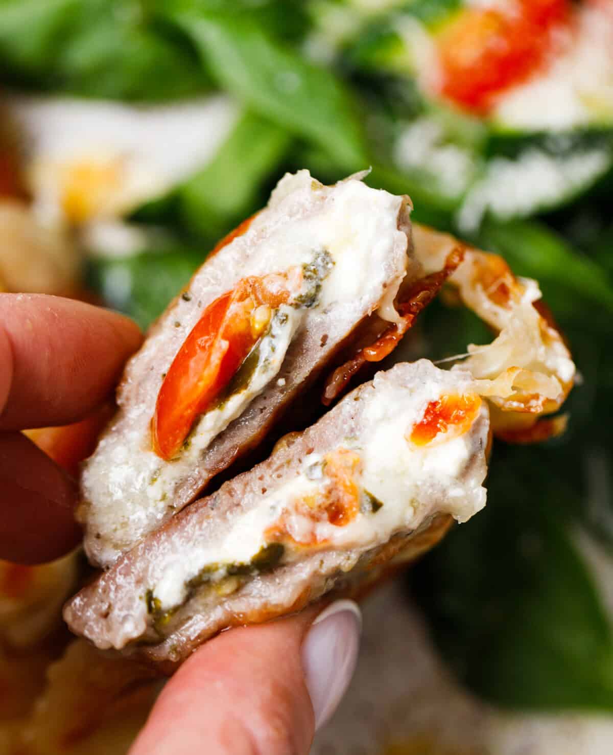 Hand holding a ground turkey pocket cut open to show cream cheese, mozzarella, spinach, and cherry tomato filling